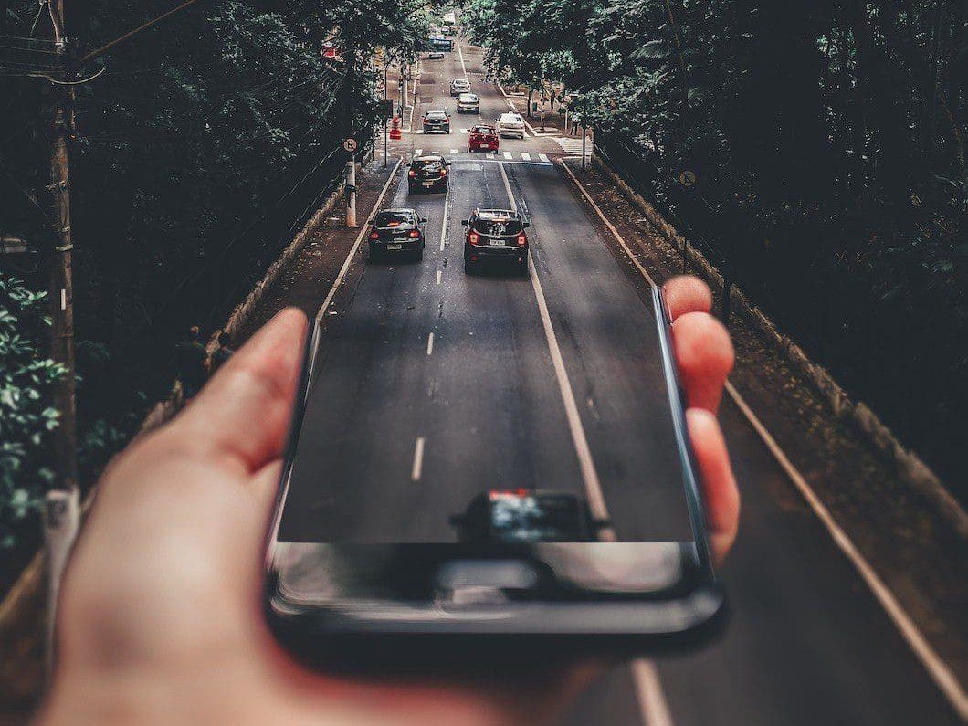 Symbolbild innovative Mobilität: Eine Hand hält ein Smartphone aus dem Auto herausfahren.