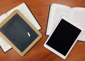 Auf dem Bild ist eine Tafel neben einem Tablet zu sehen und stellt symbolisch die digitale Bildung da.