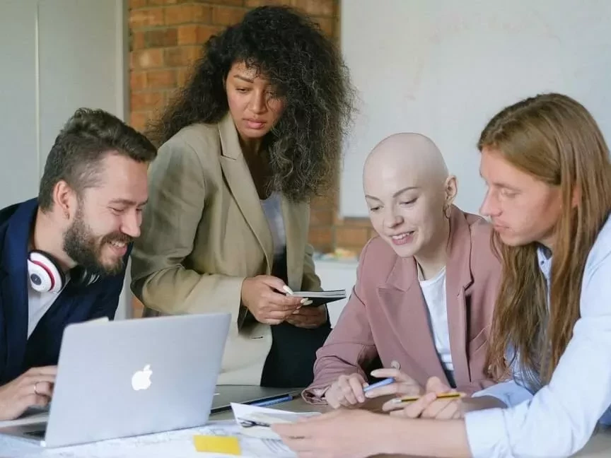 Das Bild zeigt vier diverse Personen, die gemeinsam an einem Schreibtisch sitzen und arbeiten.