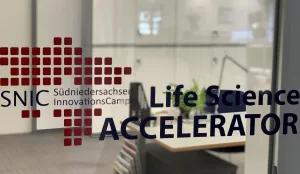 Das Bild zeigt eine Glasscheibe mit dem Logo des SNIC Accelerators. Im Hintergrund sieht man ein Büro.
