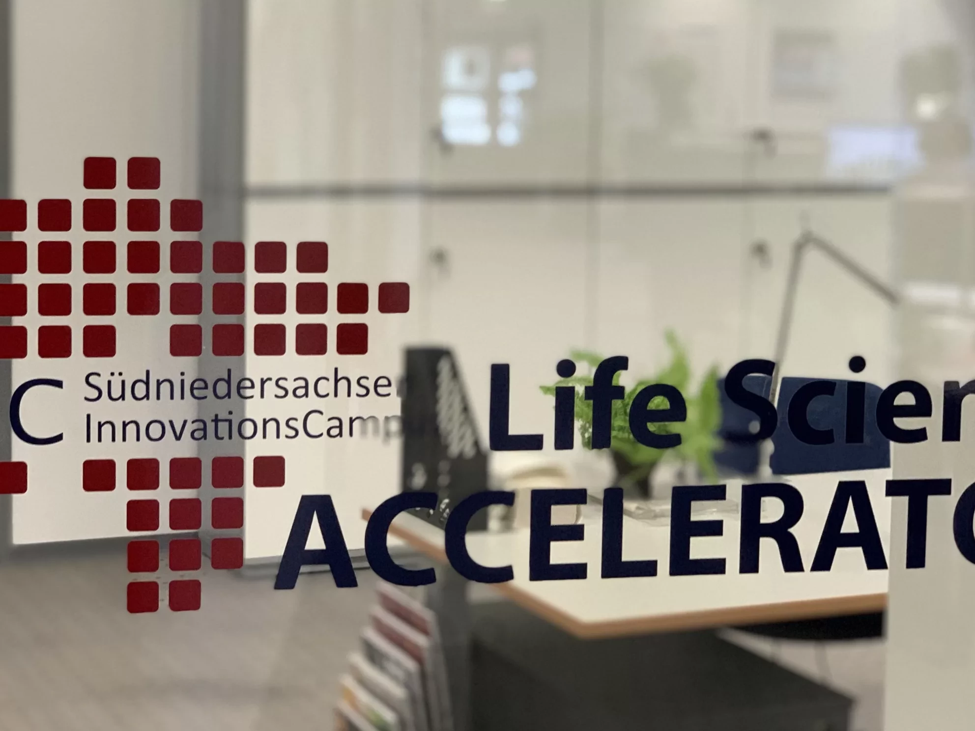 Das Bild zeigt eine Glasscheibe mit dem Logo des SNIC Accelerators. Im Hintergrund sieht man ein Büro.