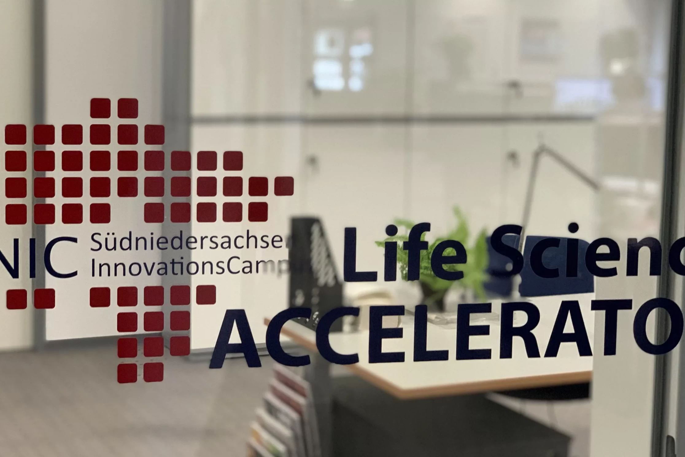 Das Bild zeigt eine Glasscheibe mit dem Logo des SNIC Accelerators. Im Hintergrund sieht man ein Büro.