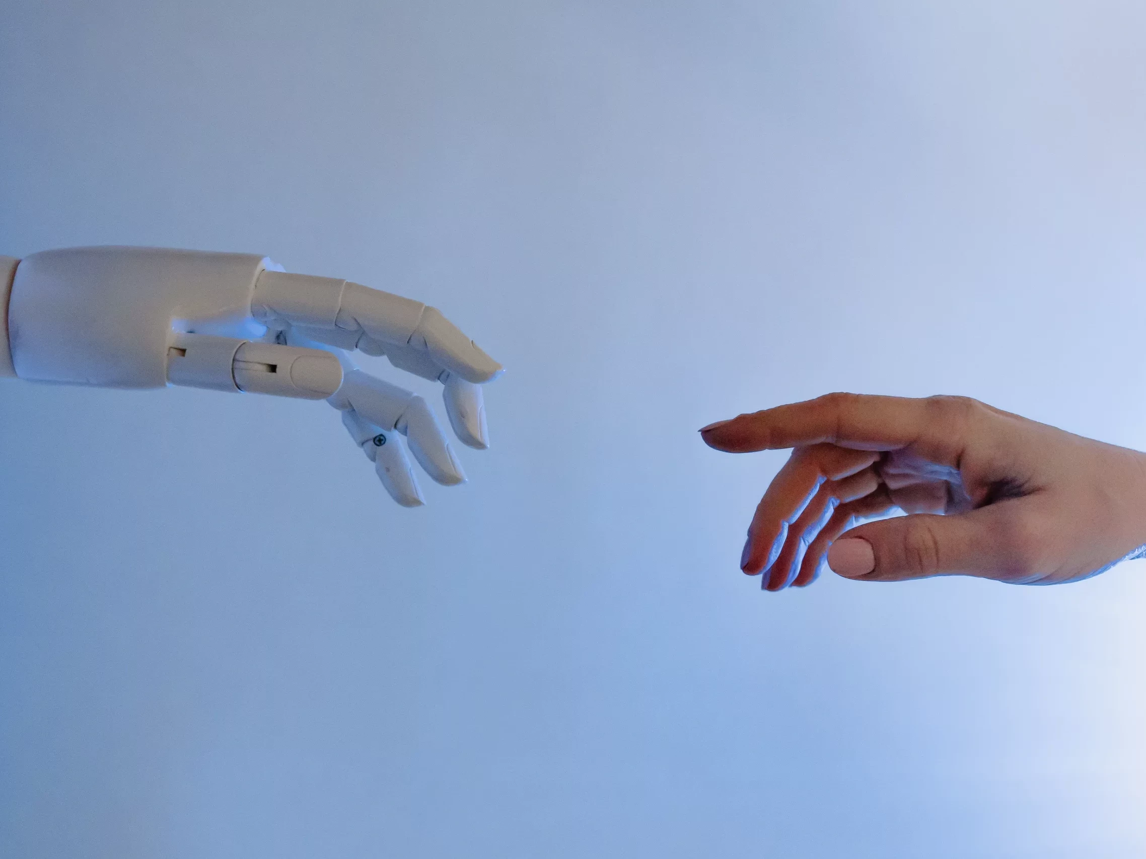 Die Hand eines Roboters und die Hand eines Menschen die aufeinander zeigen.
