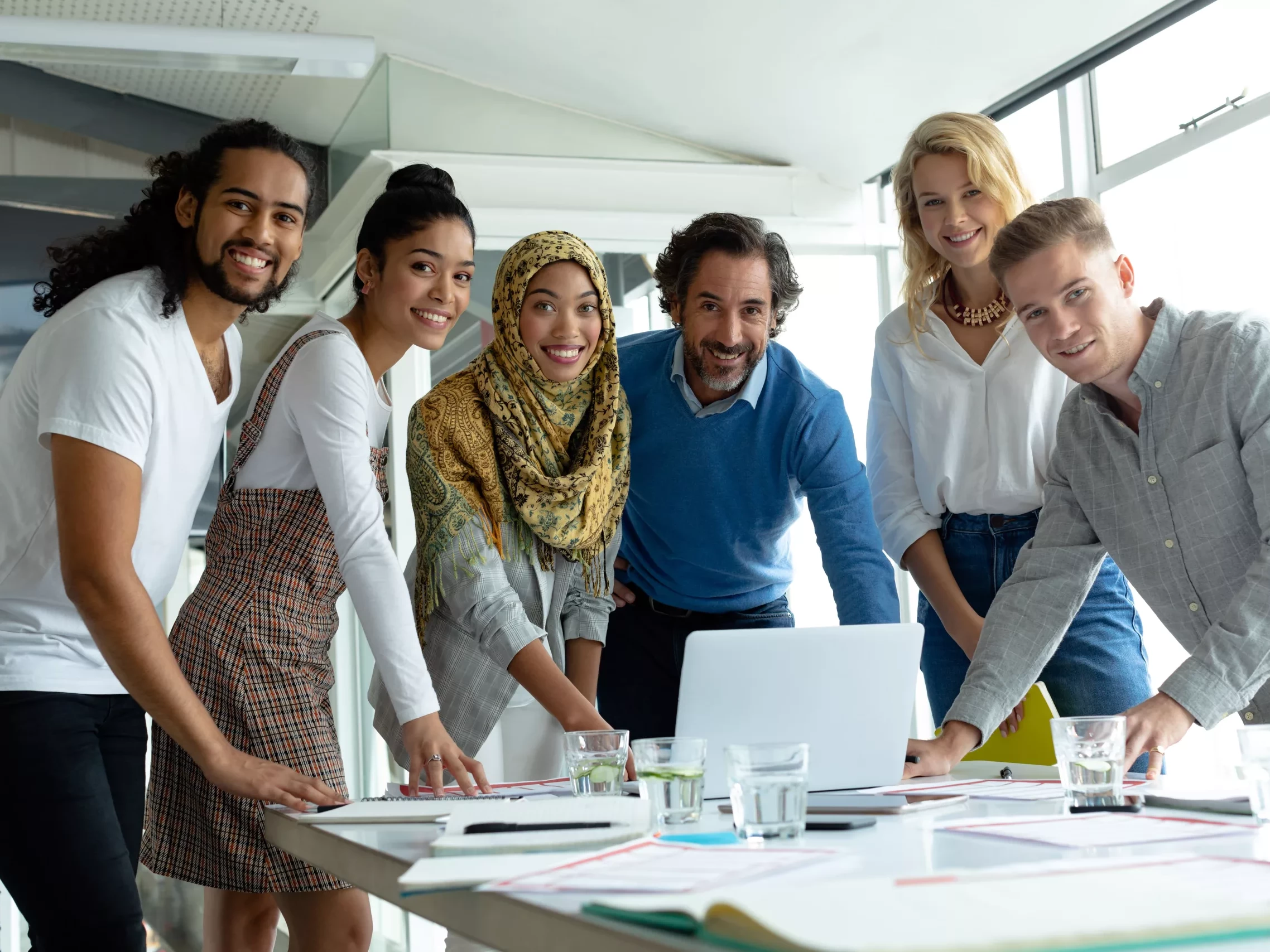 Ein diverses Team schaut in die Kamera während sie in einem modernen Besprechungsraum arbeiten.