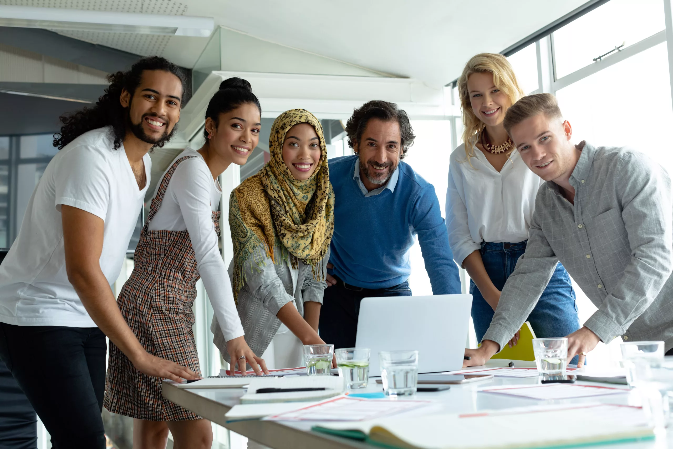 Ein diverses Team schaut in die Kamera während sie in einem modernen Besprechungsraum arbeiten.