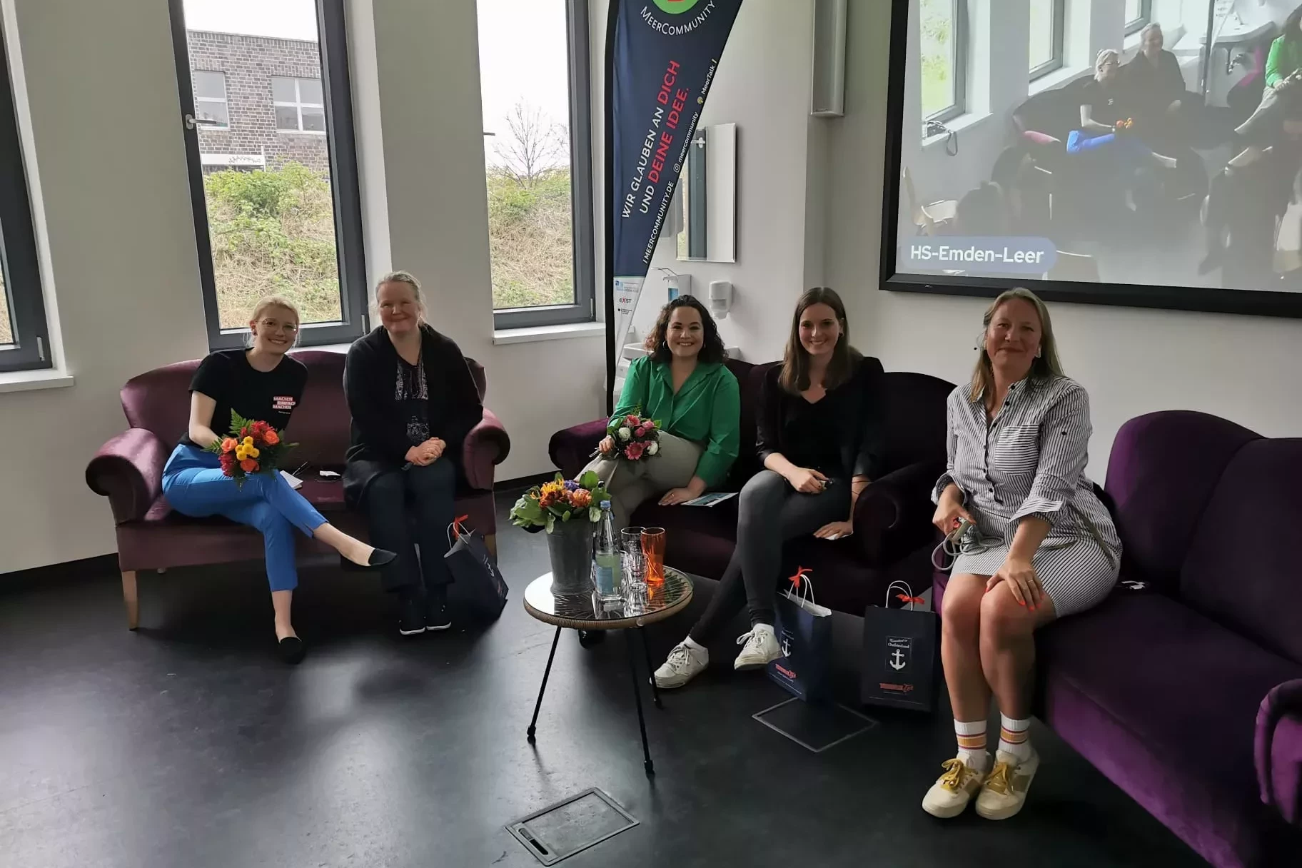 Das Bild zeigt fünf Frauen auf zwei Sofas auf einer Bühne.