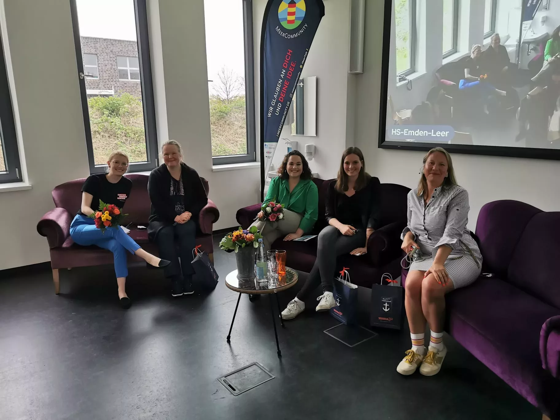 Das Bild zeigt fünf Frauen auf zwei Sofas auf einer Bühne.