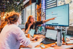 Drei Frauen vor Laptops schauen auf einen Bildschirm und besprechen sich.