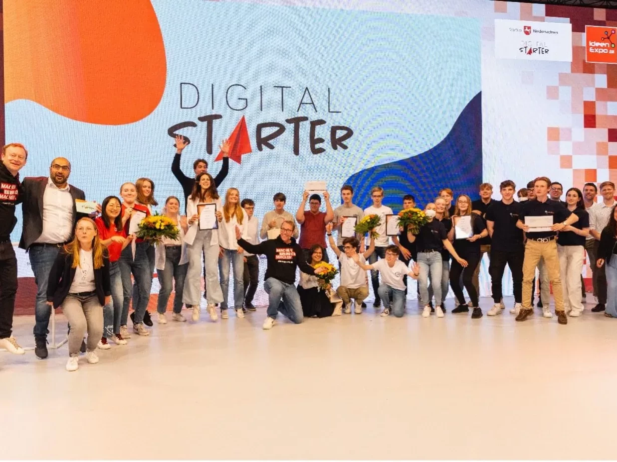 Alle Finalist*innen und Teilnehmenden stehen gemeinsam auf der Bühne vor dem DigitalSTARTer-Logo.