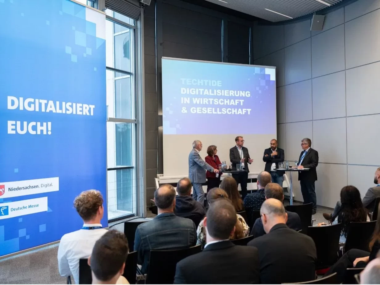 Ein Podium steht vor einem sitzendem Publikum auf der TECHTIDE.