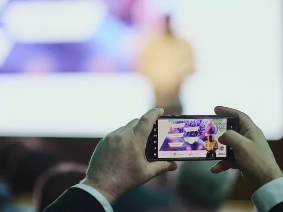 Ein Handy, dass die Bühne des Life Science Startup Days fotografiert mit dem Moderator auf der Bühne